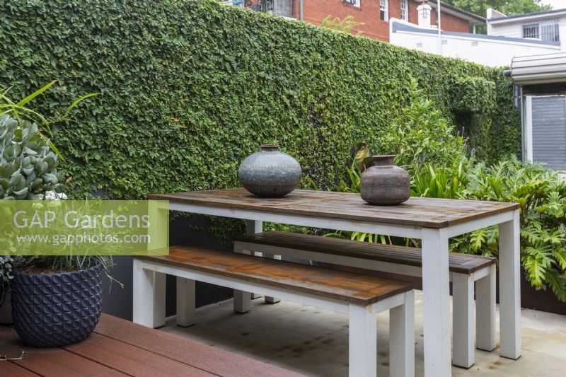 Outdoor table and bench seat with decorative hand made metal pots in an inner city courtyard garden.
