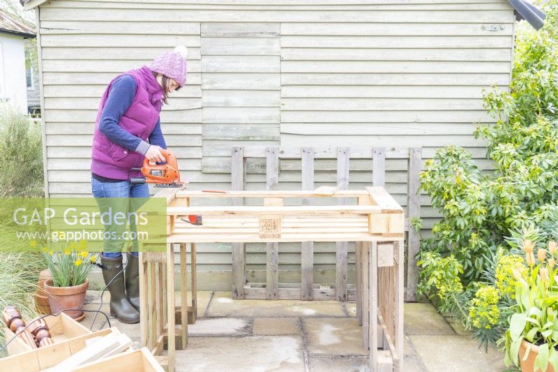 Woman cutting off excess lengths of wood from the pallet