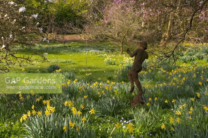 A sculpture surrounded by naturalised Narcissus and Magnolias in the Spring Garden at Thenford Arboretum.