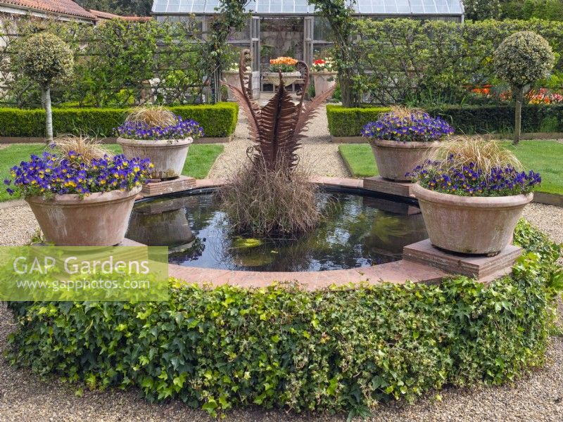Decorative raised pool with colourful containers planted with Pansies  East Ruston Old Vicarage, Norfolk. April