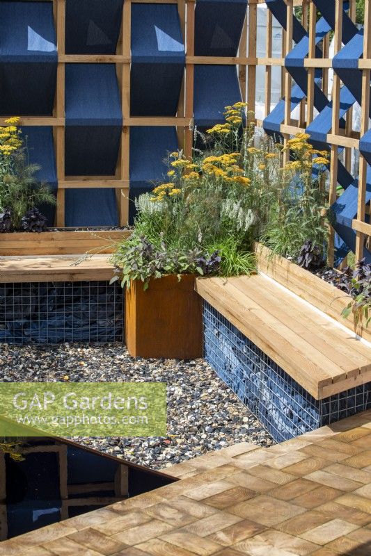 Gabion bench with wooden seat and corten steel container with planting of Achillea 'Terracotta'.  The Fashion Footprint Garden, RHS Hampton Court Palace Garden Festival 2021