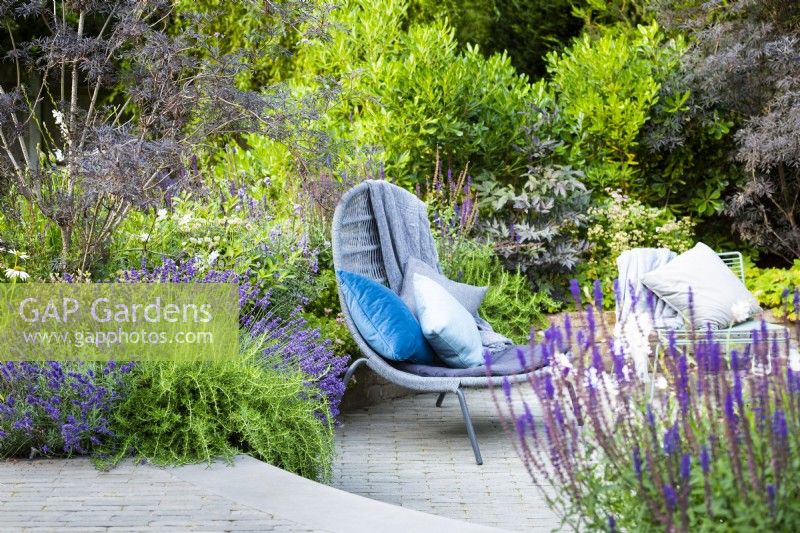 Sunken seating area with freestanding lounge chair surrounded by Lavendula, Rosmarinus and Salvia nemorosa 'Caradonna'.