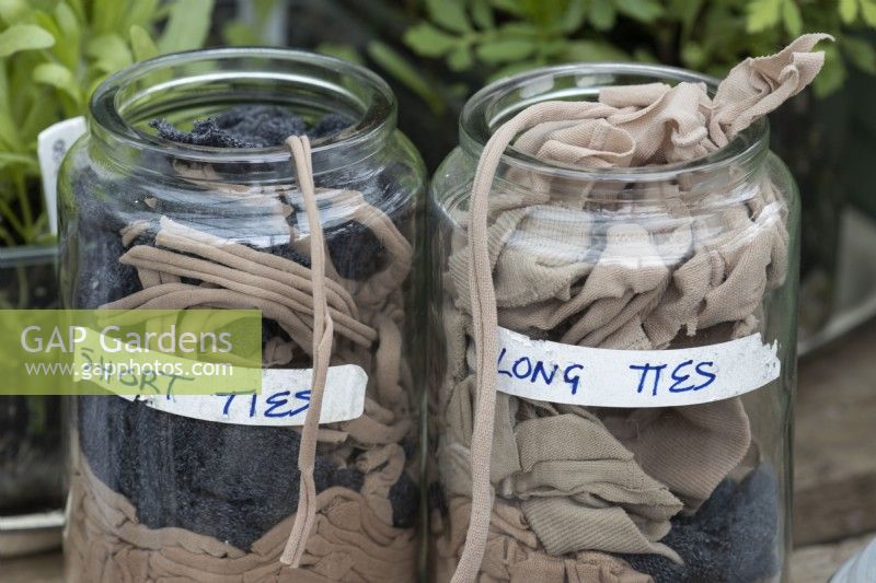 Old tights cut up into strips make ties for use in the garden. The ties are used to tie up climbing plants and are stored in mason jars. There are two lengths, long and short ties each in their own storage jar. 