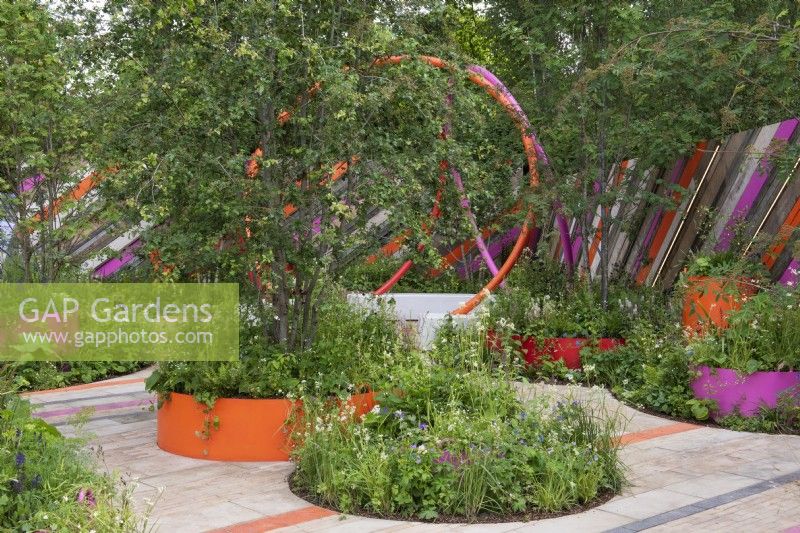 In a design for a miniature urban park, giant round planters are filled with native rowan and hawthorn trees, above layered textural foliage punctuated with floral accents.