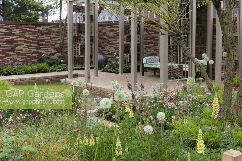 A pavilion crafted from woven willow screens overlooks a sunken pool edged in herbaceous beds planted with a tapestry of lupins, alliums, geums, astrantias, pimpinella, verbascums and ornamental grasses.