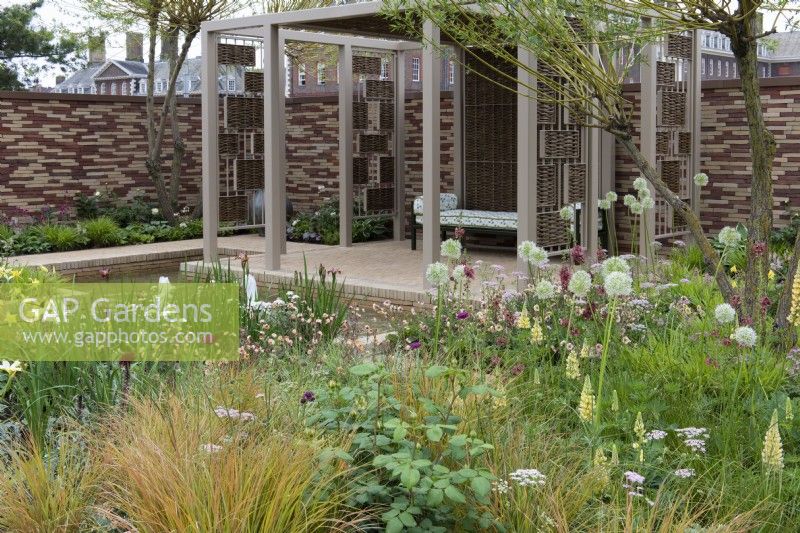 A pavilion crafted from woven willow screens overlooks a sunken pool edged in herbaceous beds planted with a tapestry of lupins, alliums, geums, astrantias, pimpinella, verbascums and ornamental grasses. 