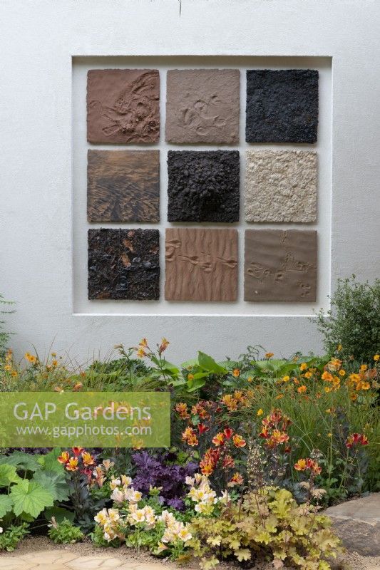 A wall panel features clay tiles, the colours reflected in the border below with purple Heuchera 'Chocolate Ruffles' and Alstroemeria 'Inca Safari'.