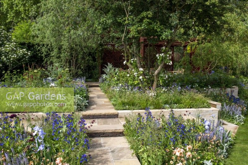 Yorkstone paved path with handmade clay tile risers, leads through planting beds to a laser cut pavilion - Morris  and  Co, RHS Chelsea Flower Show 2022 - Gold Medal