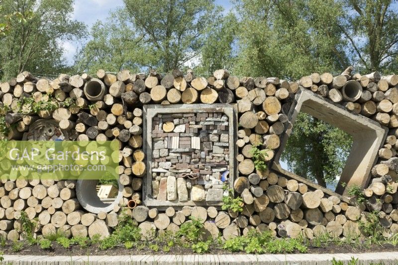 Insects hotels made in wall of stacked tree trunks and concrete drainage pipes. 