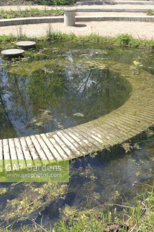 Pond in which the pavement disappears as a spiral into the water filled with plants.