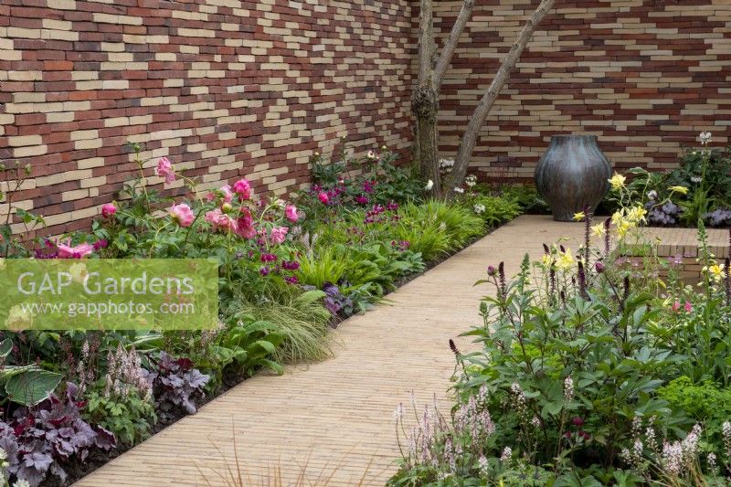 Border next to a clay paver path with Paeonia 'Coral Sunset',  Rose 'Queen of Sweden', Tiarella 'Pink Skyrocket' and Hakonechloa macra - The Stitcher's Garden, RHS Chelsea Flower Show 2022 - Silver Medal