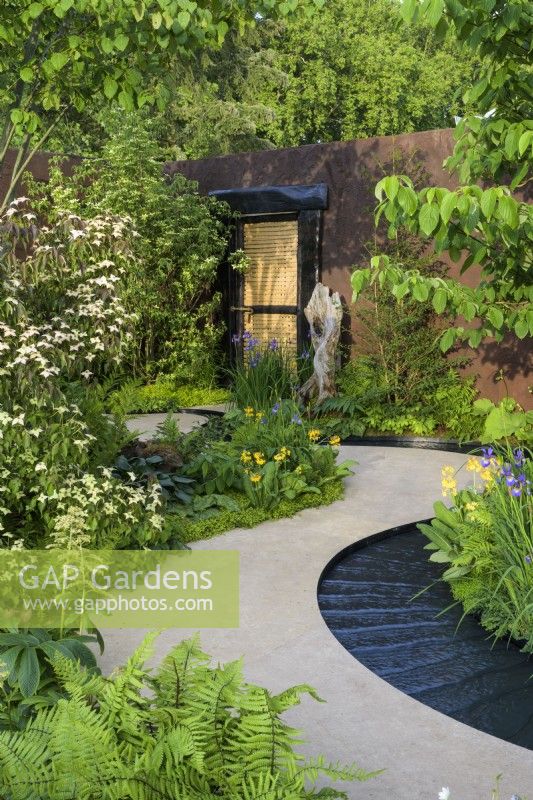 Curved path leading to doorway and water rill around  bed planted with Cornus kousa var. chinensis above shade-loving hostas, primulas, irises and disporum - The Boodles Travel Garden