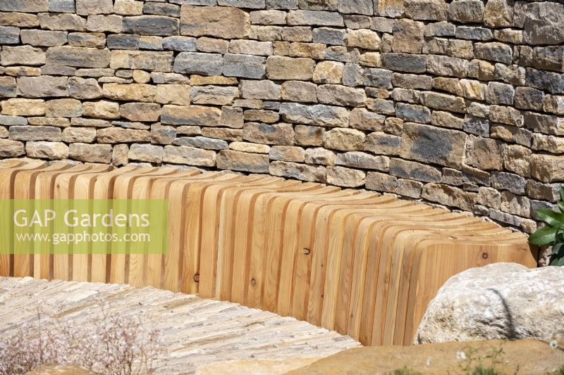Curved slatted bench next to a dry stone wall - The RAF Benevolent Fund Garden, RHS Chelsea Flower Show 2022 - Silver Medal