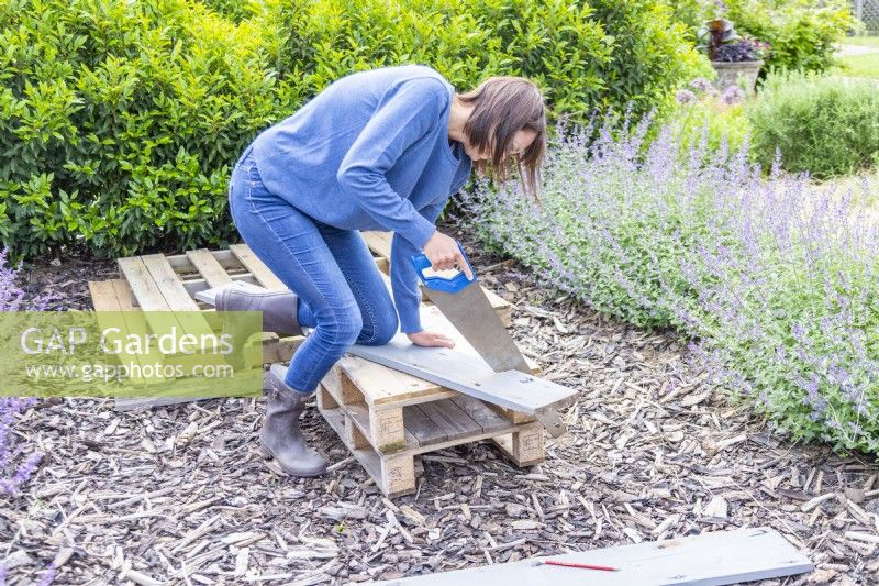 Woman sawing the wooden planks at an angle to fit on the pallet dog bed 