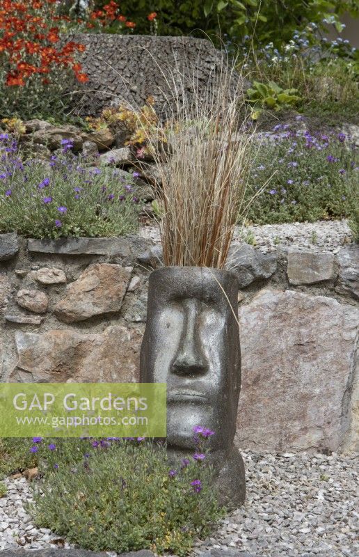 Easter Island style sculptural head planted with ornamental grass to add interest to terracing. Spring