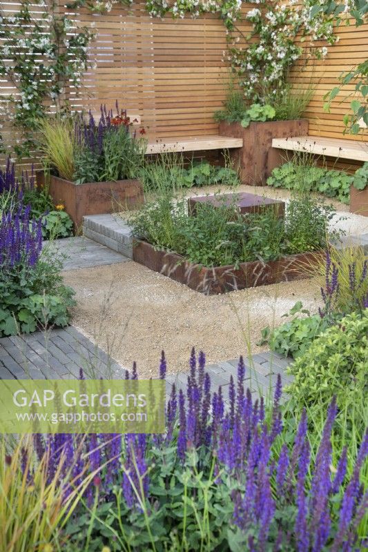 Simple wooden benches overlook a reflective water feature in Lunch Break Garden at RHS Hampton Court Palace Garden Festival 2022