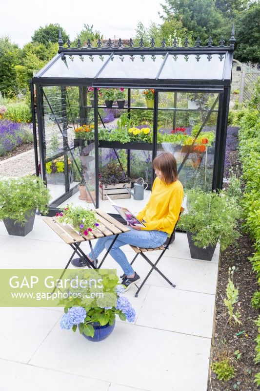 Woman reading magazine outside of small greenhouse