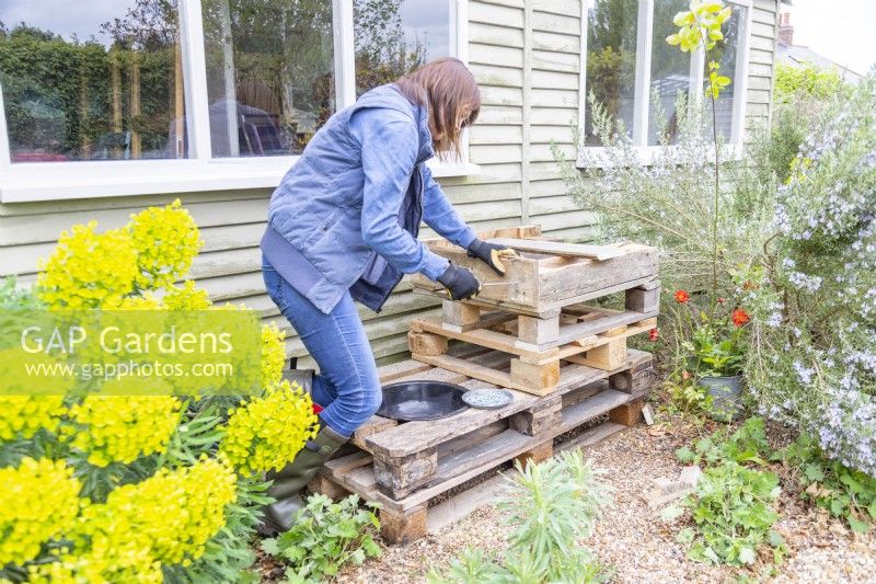 Woman screwing the plank of wood to the side of the pieces of pallet