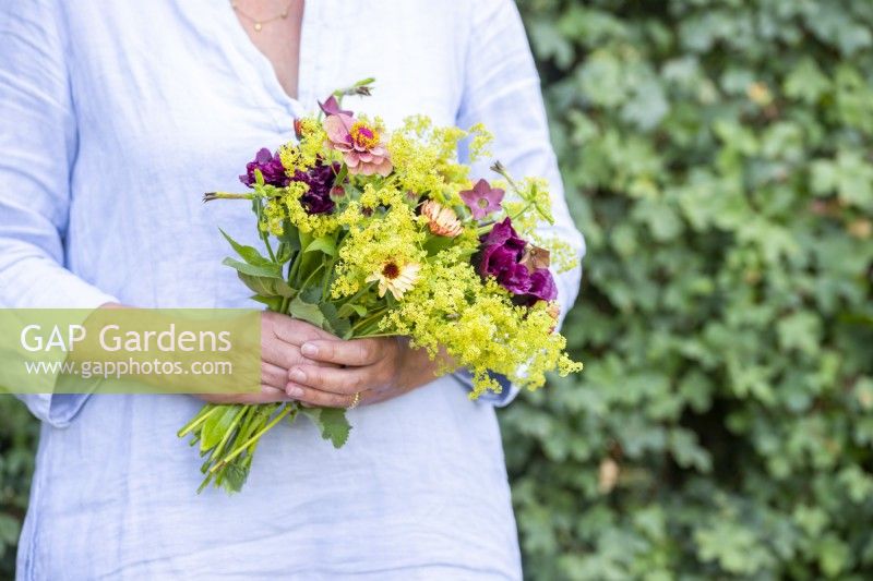 Woman holding a bouquet containing Calendula 'Sherbet Fizz', Papaver paeoniflorum 'Black Peony', Poppy Seed pods, Nicotiana 'Bronze Queen', Alchemilla mollis and Zinnia 'Queen Red Lime'