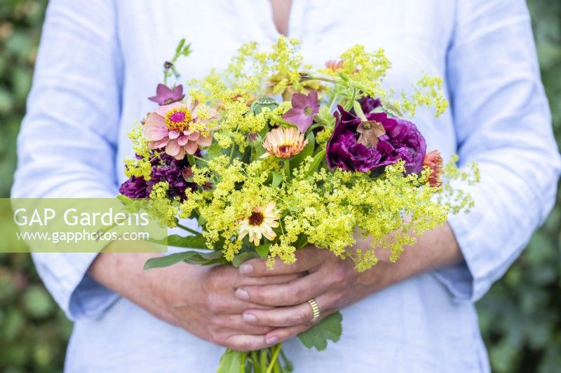 Woman holding a bouquet containing Calendula 'Sherbet Fizz', Papaver paeoniflorum 'Black Peony', Poppy Seed pods, Nicotiana 'Bronze Queen', Alchemilla mollis and Zinnia 'Queen Red Lime'