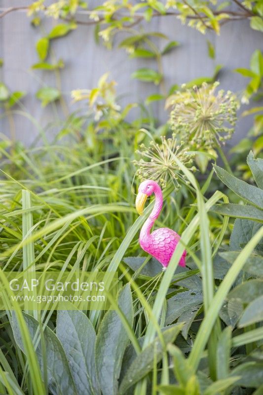 Small flamingo ornament among various plants in a border