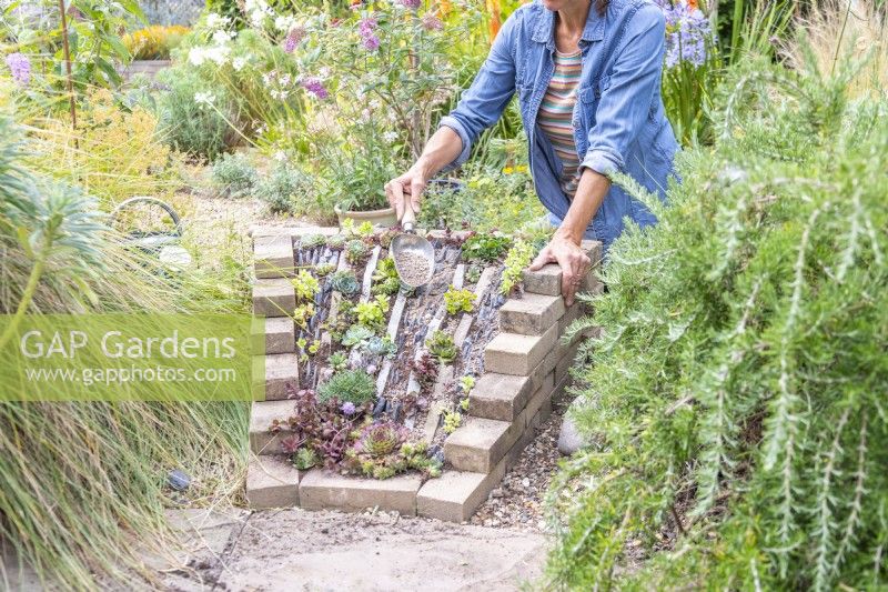 Woman covering the compost in the sloped crevice garden with gravel