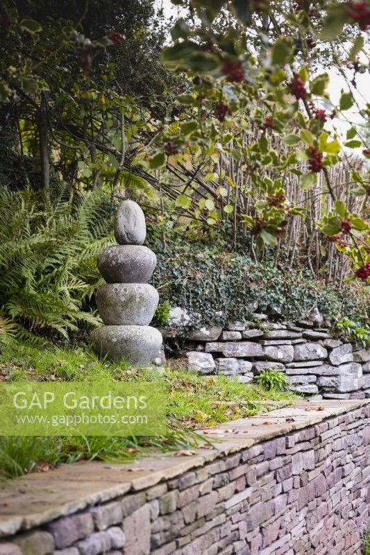 A tower of three Ming dynasty column bases topped with a river pebble in a country garden in November