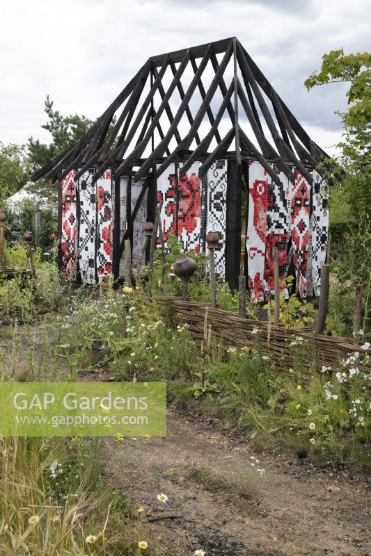 Burnt out Ukrainian Cottage in a field of barley in the What Does Not Burn garden at RHS Hampton Court Palace Garden Festival 2022