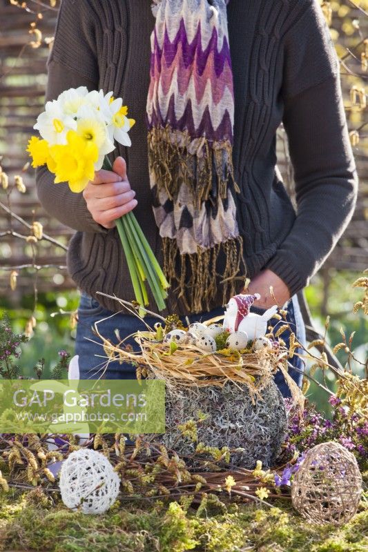 Woman creating outdoor Easter arrangement with straw nest and quail eggs.
