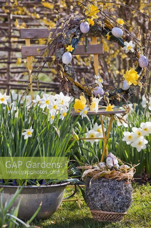 Outdoor Easter decoration with egg nest and hanging wreath. Pots of daffodil - Narcissus - in foreground.