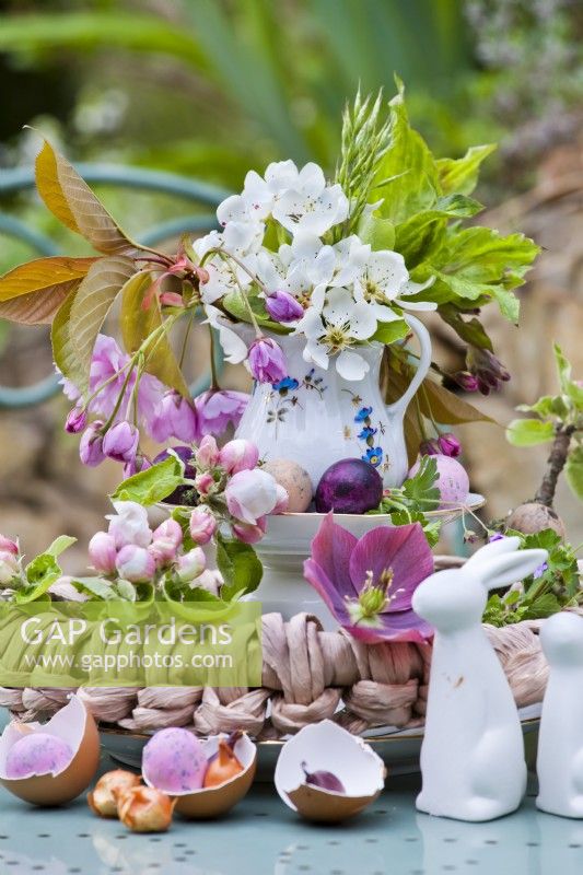 Spring flowers arranged on tiered stand for Easter - cherry blossom twigs, eggs and rabbit ornaments.