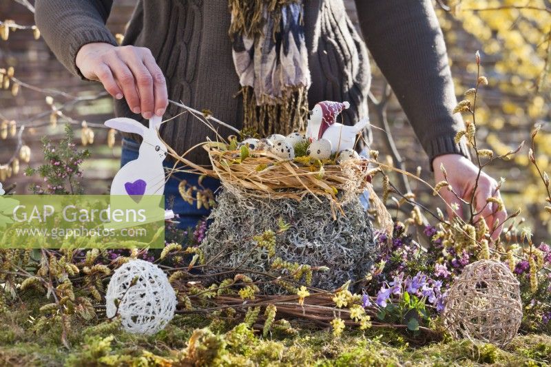Woman creating outdoor Easter arrangement with straw nest and quail eggs.