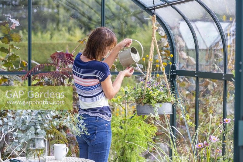 Woman in greenhouse watering small hanging planter