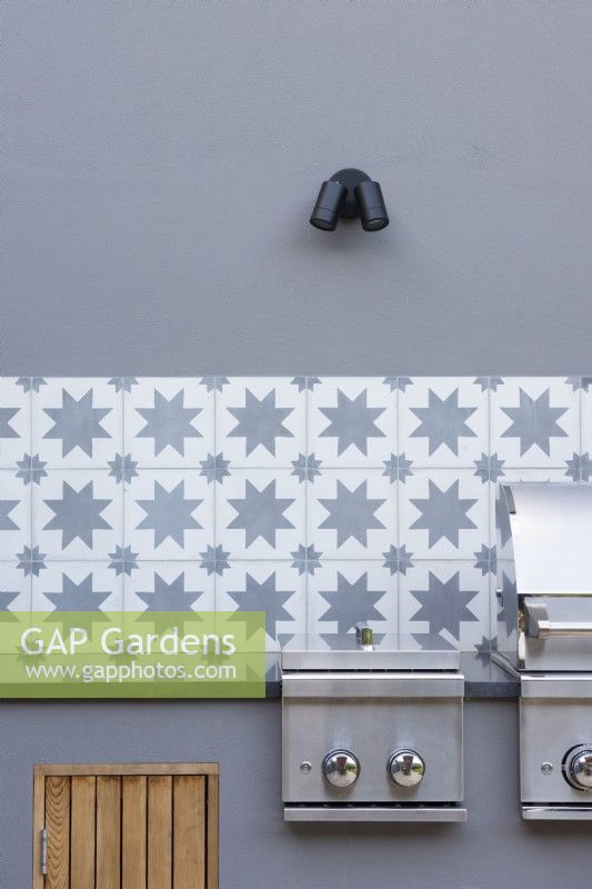 Detail of outdoor kichen with grey walls, decorative wall tiles and bbq. 