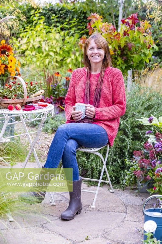 Woman sitting at a table on a patio with a hot drink, surrounded by plants