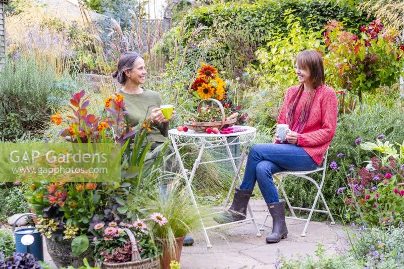 Women sitting at a table and chatting on stone patio surrounded by plants