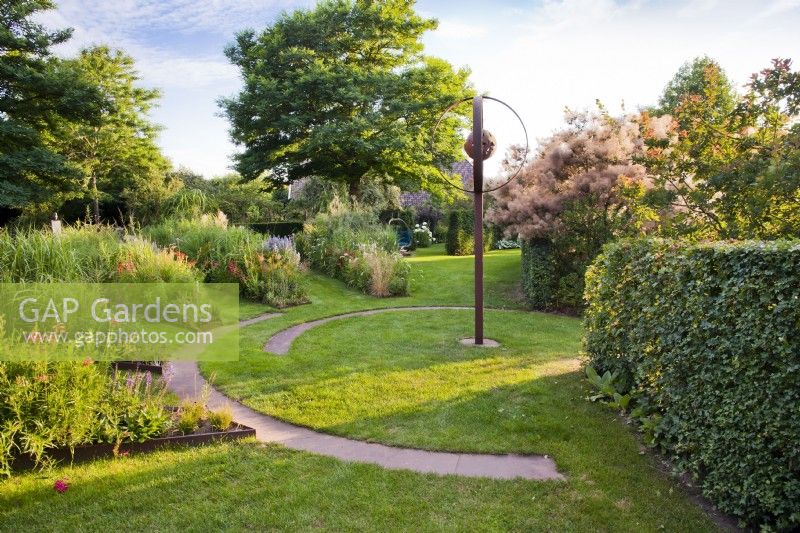 Circular garden with steel edged herbaceous borders, lawn and circular path.