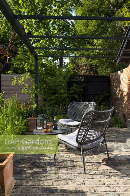 Seating area with metal chairs, a table and pergola. 