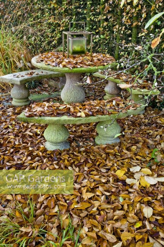 Stone furniture covered with fallen autumn leaves.