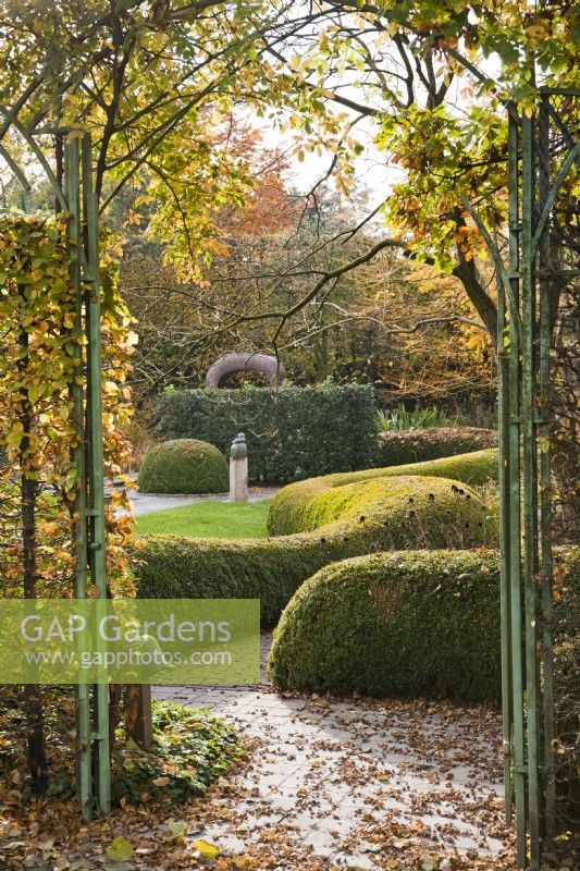 Wrought iron arched garden gate with path leading to the part with box topiary hedging.