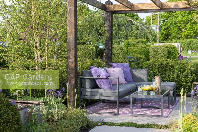 Seating area under a wooden pergola surrounded by Betula and evergreen hedging - Abigail's Footsteps, RHS Malvern Spring Festival 2022