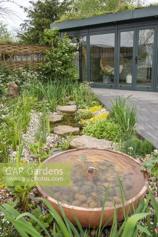 Decking leading to a home office, next to copper water feature and gravel planting - The Hide Garden, RHS Malvern Spring Festival 2022