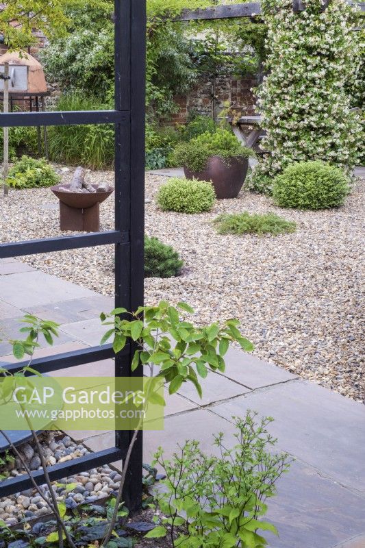 View across small Oriental inspired small garden with evergreen shrubs growing in the gravel and wooden arbor