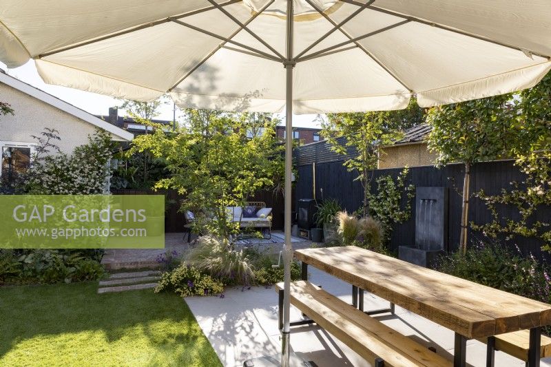 Seating area with parasol and wooden table with bench in small suburban garden