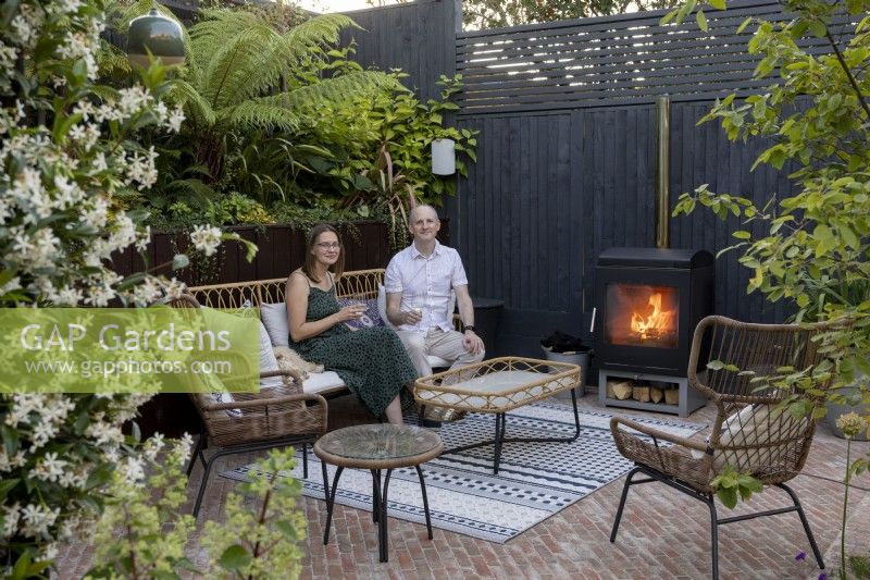 Man and lady sitting in patio area next to log burner in suburban garden