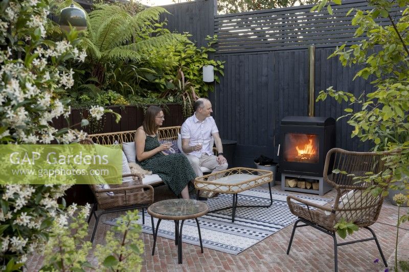 Man and lady sitting in patio area next to log burner in suburban garden
