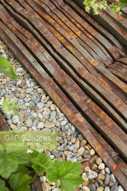 Detail of border edge using pebbles and Medite Smartply, a sustainable and innovative wood-based panel product that resembles rusting metal.