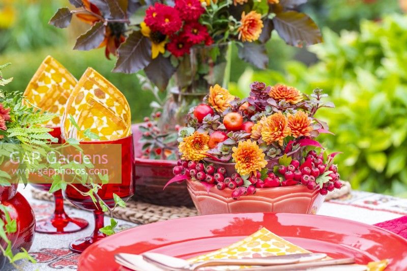 Bowl containing chrysanthemums, crab-apples, succulents and berries next to red tableware set