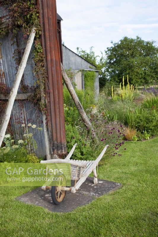 View of a vintage wooden wheelbarrow in the garden at the Cottage Herbery with further back a mixed border.