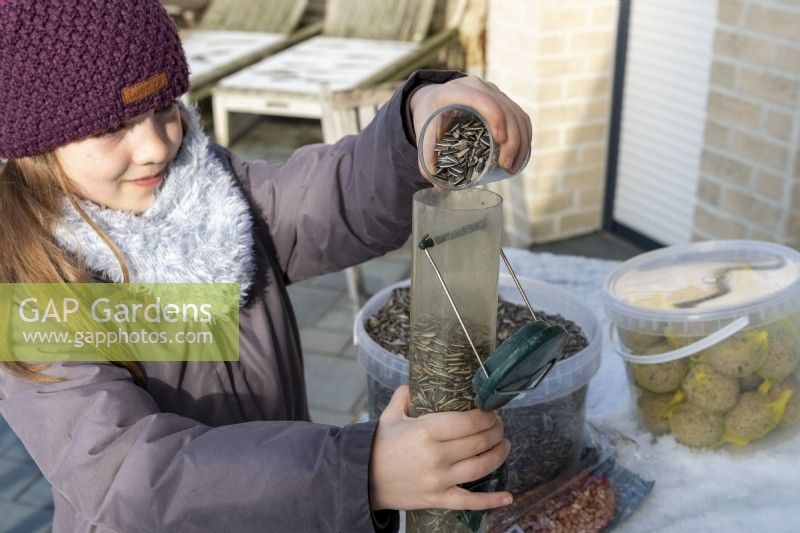 Girl filling bird feeder with sunflower seeds on snowy day in winter